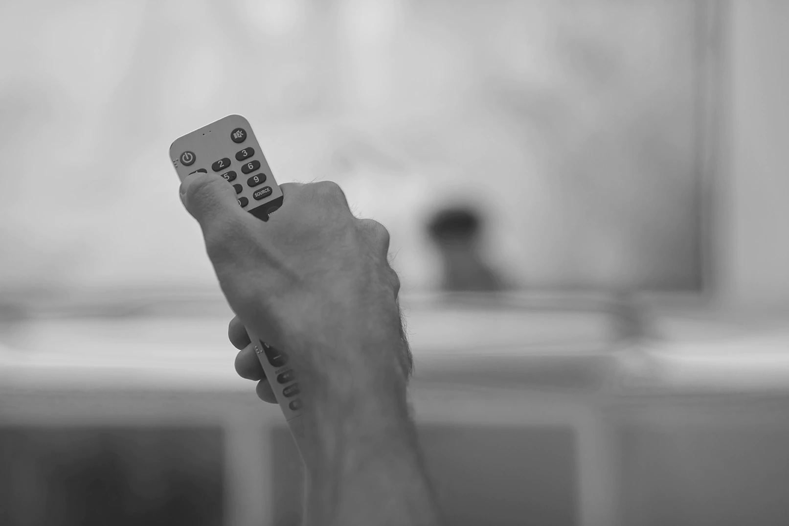 Hand betätigt Fernbedienung vor hellem, verschwommenen Hintergrund